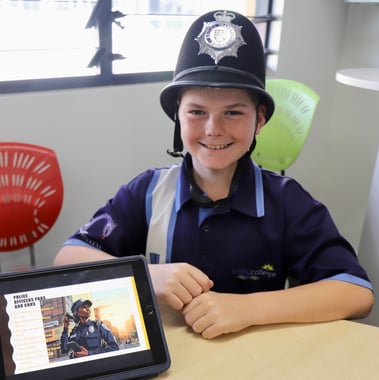 A student in primary school wearing a pilice helmet with an ipad with a project about what police officers do