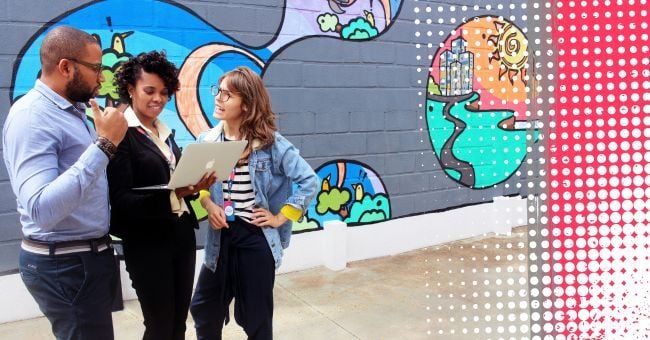 Three teachers having an animated conversation in front of a wall of colourful graffiti