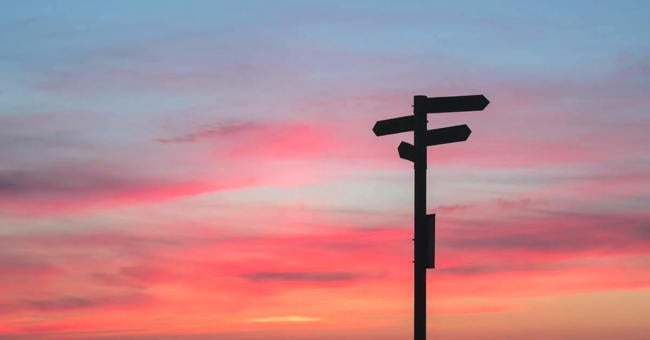A signpost is silhouetted against the colours of a dawn sky