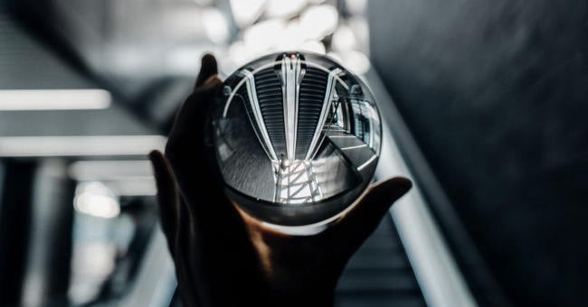 A round glass ball like a crystal ball in a hand held up to the sky in a grey setting