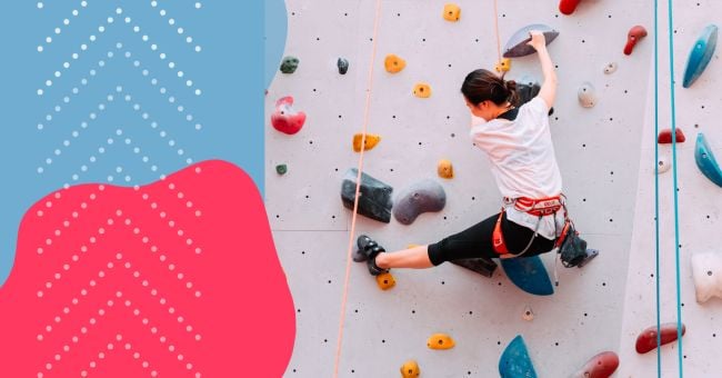 A climber on a white climbing wall with colourful hand and foot holds and ropes