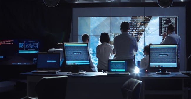 Several people in a control room seen from the back. 