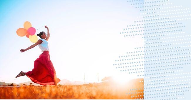 A woman running in the sunshine with a handful of brightly coloured balloons