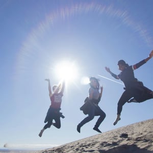 three teenagers jumping with joy on a sunny beach