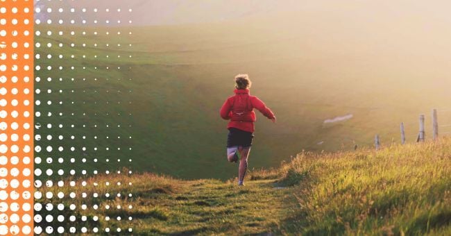 A runner in bright sunlight running down a country track. They are wearing a red jacket. 