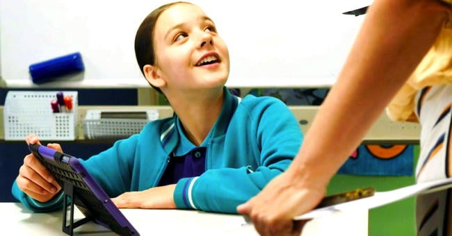 A girl with a tablet smiles at her teacher