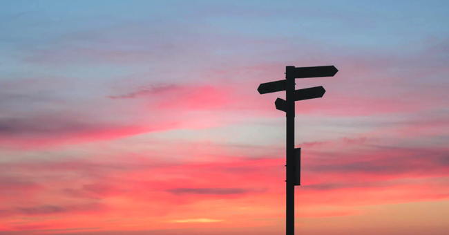 A signpost is silhouetted against the colours of a dawn sky