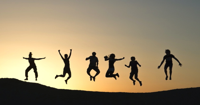 Silhouette of several people jumping against a yellow dawn sky. 
