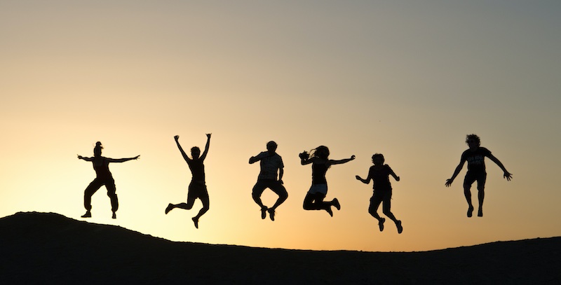 Silhouette of several people jumping against dawn sky. 