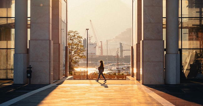 A woman walks between two city buildings in the sunshine