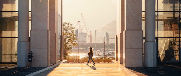 A woman walks between two city buildings in the sunshine