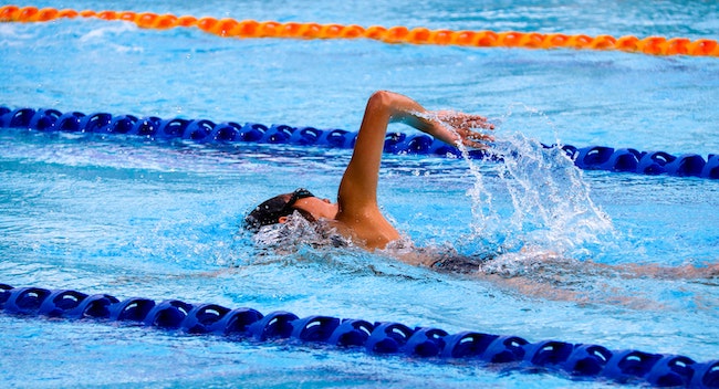 A swimmer doing laps. Image shows a blue pool with blue and orange ropes and a person doing front crawl between two ropes.